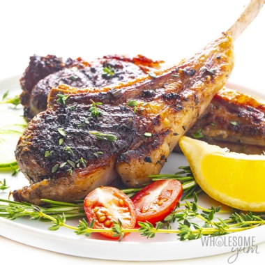 Oven baked lamb chops on a plate with lemon wedges and sliced grape tomato