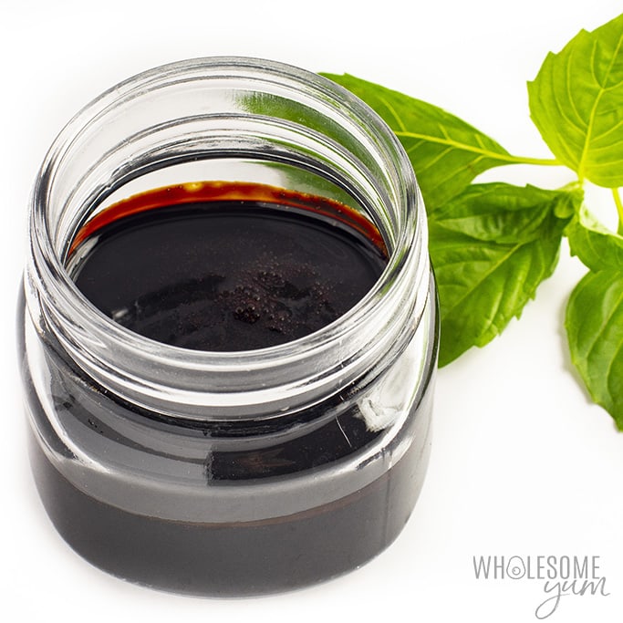 Balsamic glaze in a glass jar with a basil cluster next to it