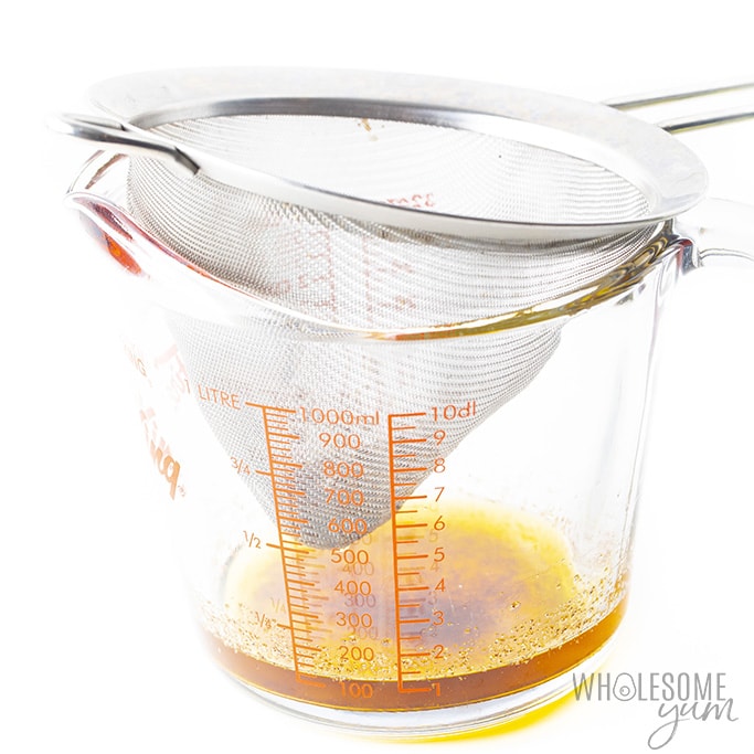 Lemon butter sauce being strained through a fine mesh sieve into a measuring cup