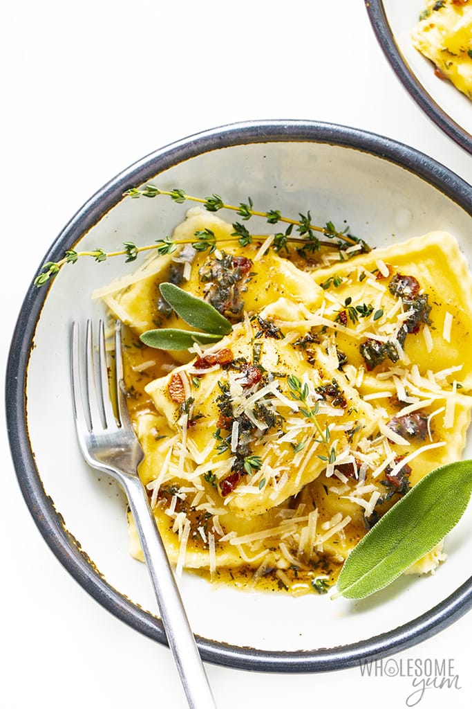 Low carb ravioli filled with butternut squash in a bowl with a fork and topped with Parmesan cheese and sage