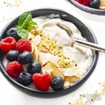 Keto yogurt in a bowl with fruit, a spoon and other toppings.