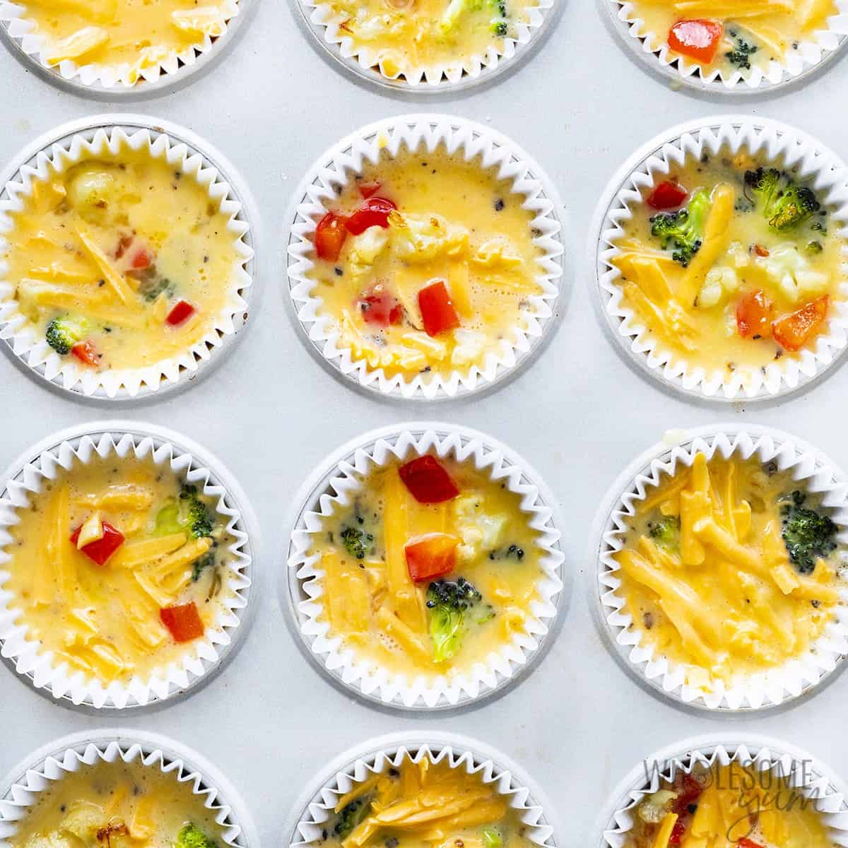 Egg muffin cups in a muffin tin, filled before baking.