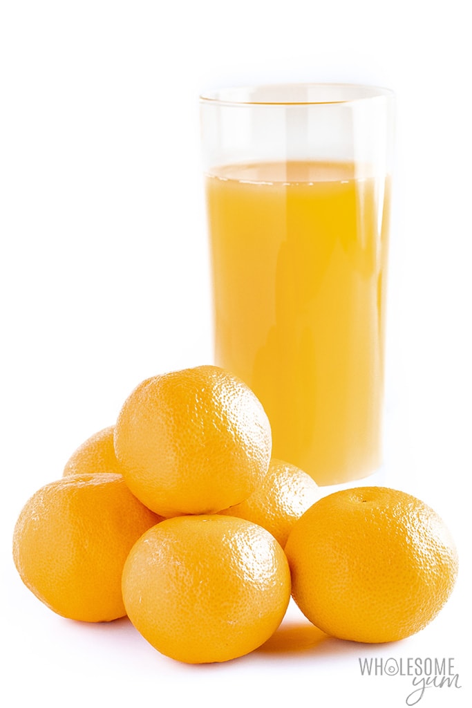 Glass of orange juice next to a pile of oranges. 