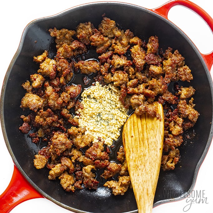 Sausage in a skillet with well of garlic in the center