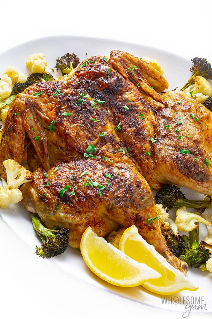 Roasted spatchcock chicken recipe with vegetables and lemon wedges
