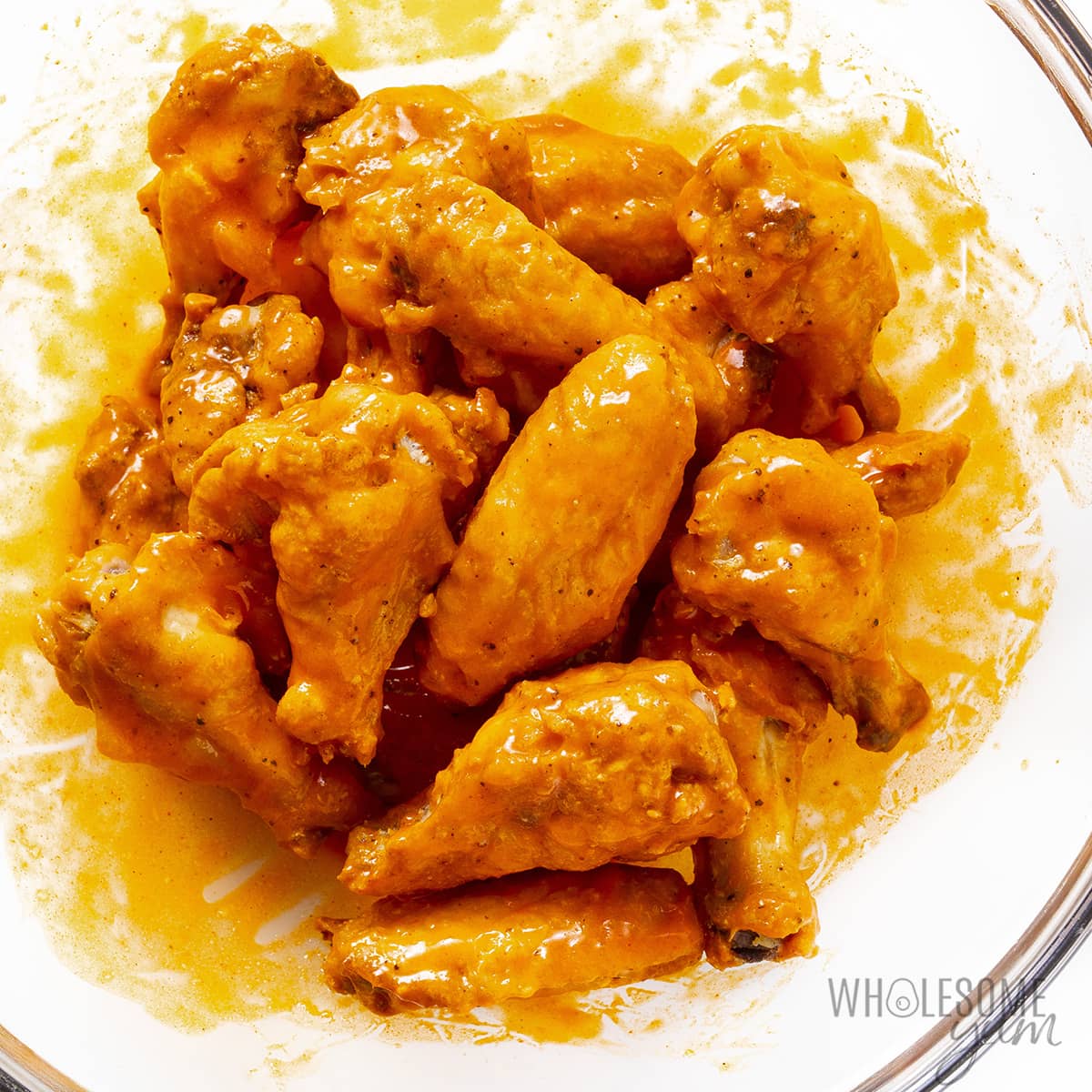 Wings tossed in the buffalo sauce in a bowl.