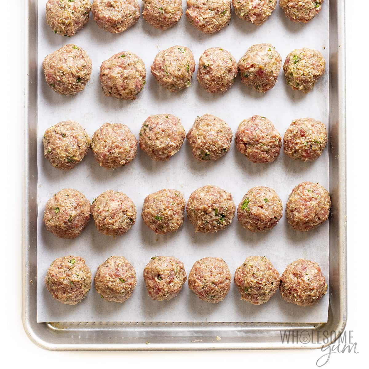 Meatballs rolled into balls on baking sheet with parchment paper. 