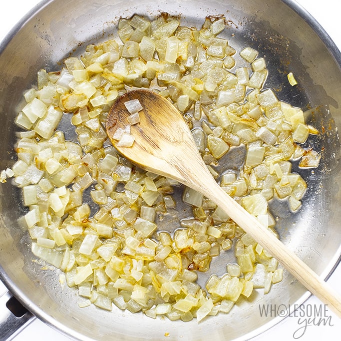 Sauteed onions in a skillet with a wooden spoon