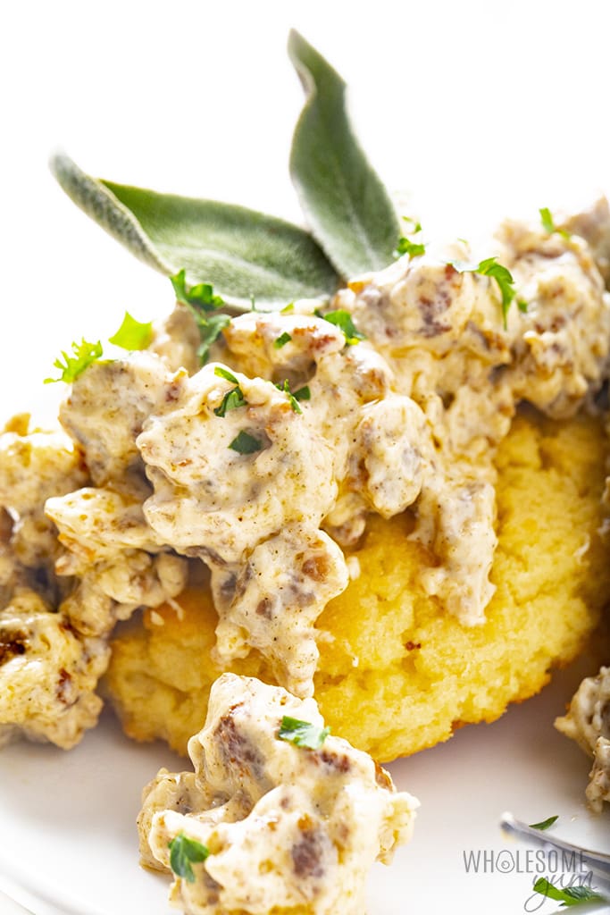 Close up biscuit with low carb sausage gravy and sage leaf on top