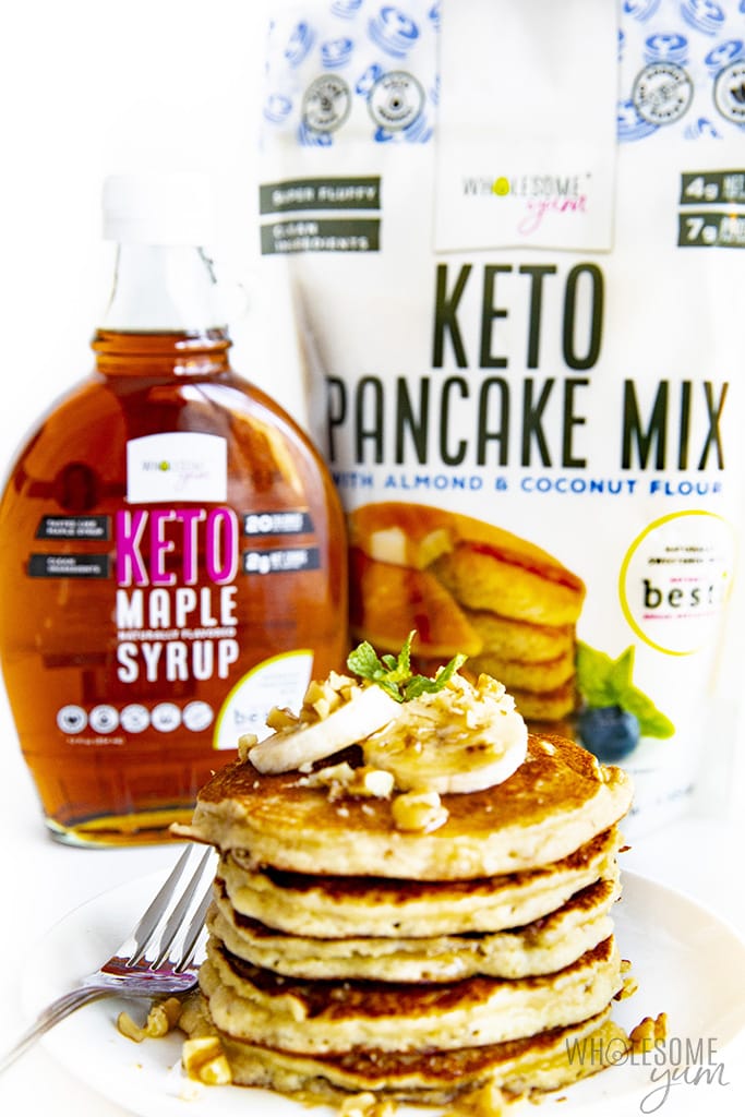 Stack of keto banana pancakes with a bag of Wholesome Yum Pancake Mix and Keto Maple Syrup