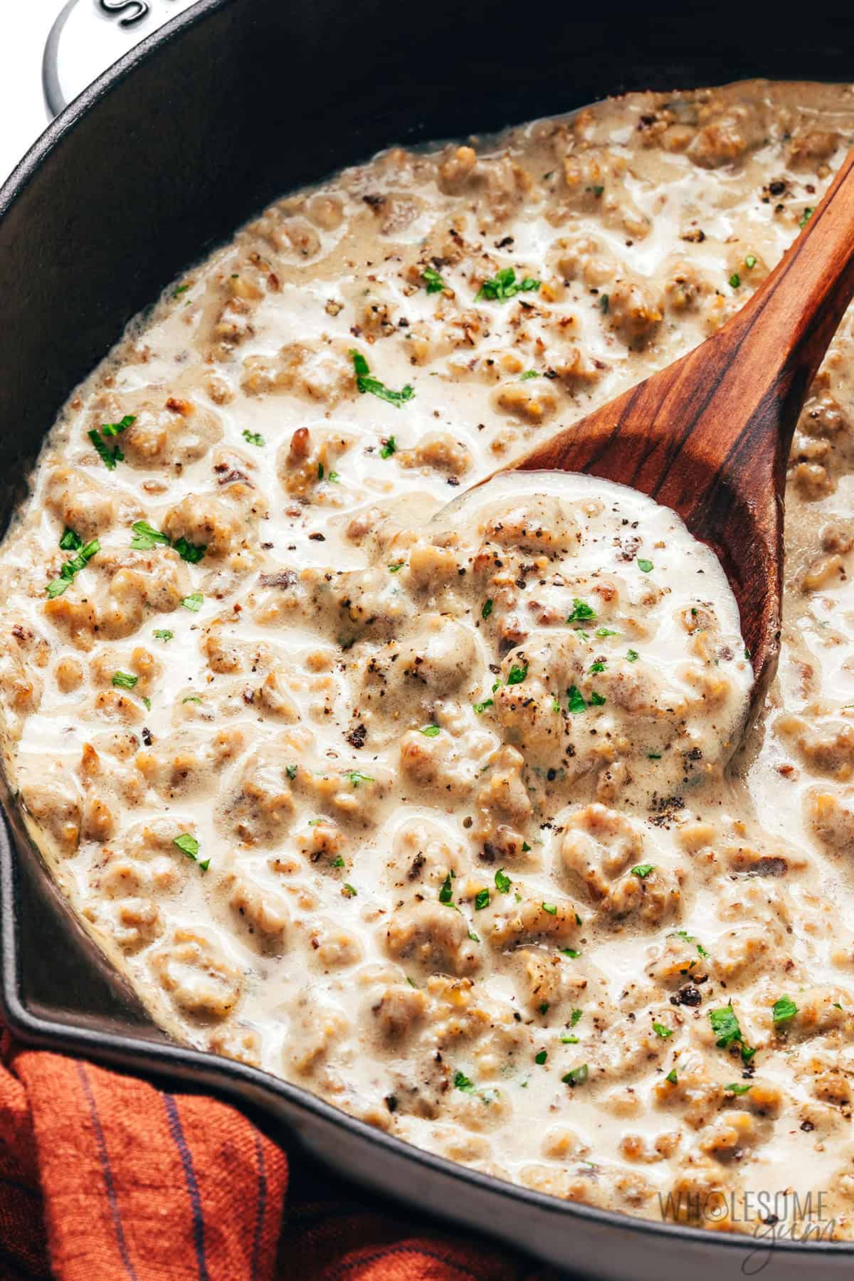 Rich, creamy sausage gravy in a skillet with a wooden spoon.