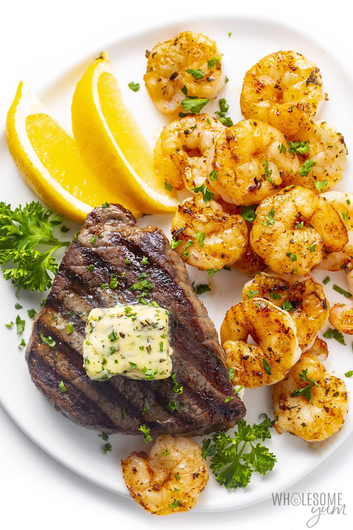 Steak and shrimp on a plate with lemon wedges.