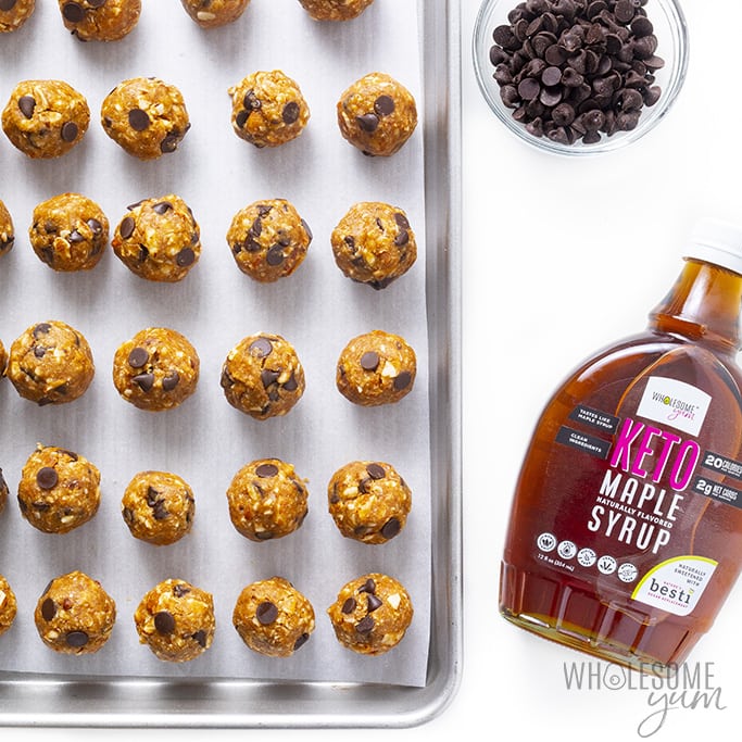 Low carb energy balls on baking sheet with a bottle of keto maple syrup