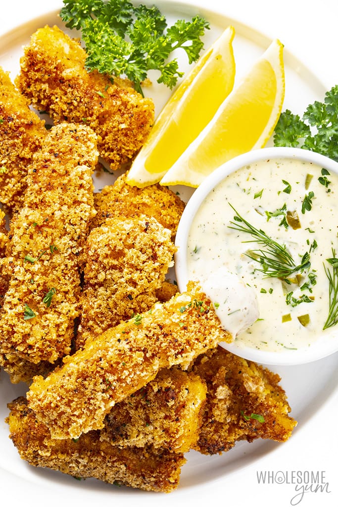 Plate of keto fish sticks with one fish stick dipped into a dish of tartar sauce
