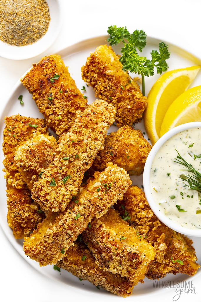 Fish sticks on a plate next to tartar sauce and lemon wedges