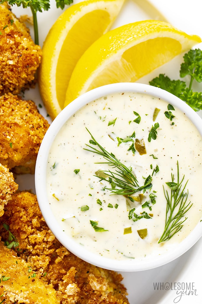 Keto tartar sauce in a bowl garnished with herbs, next to fish sticks