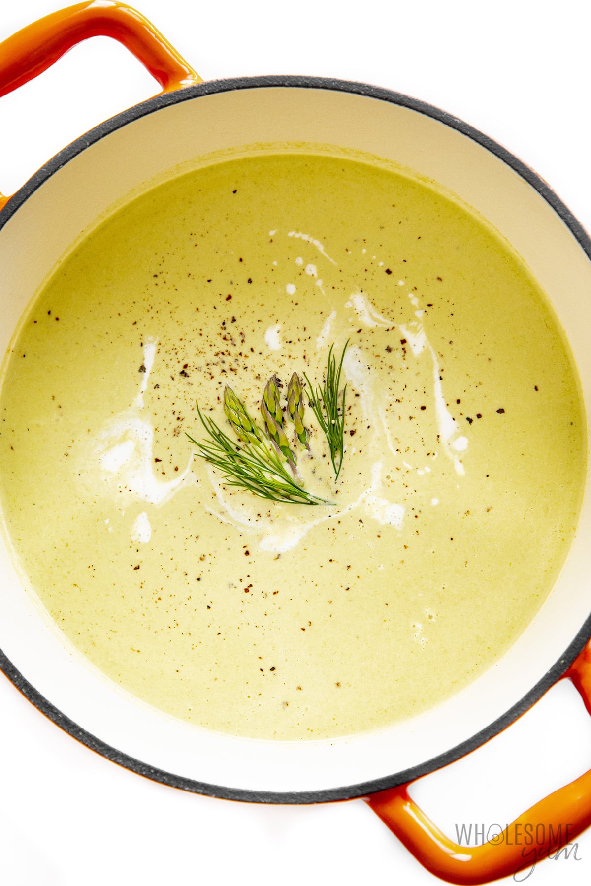 Cream of asparagus soup garnished with herbs and cream in a Dutch oven.