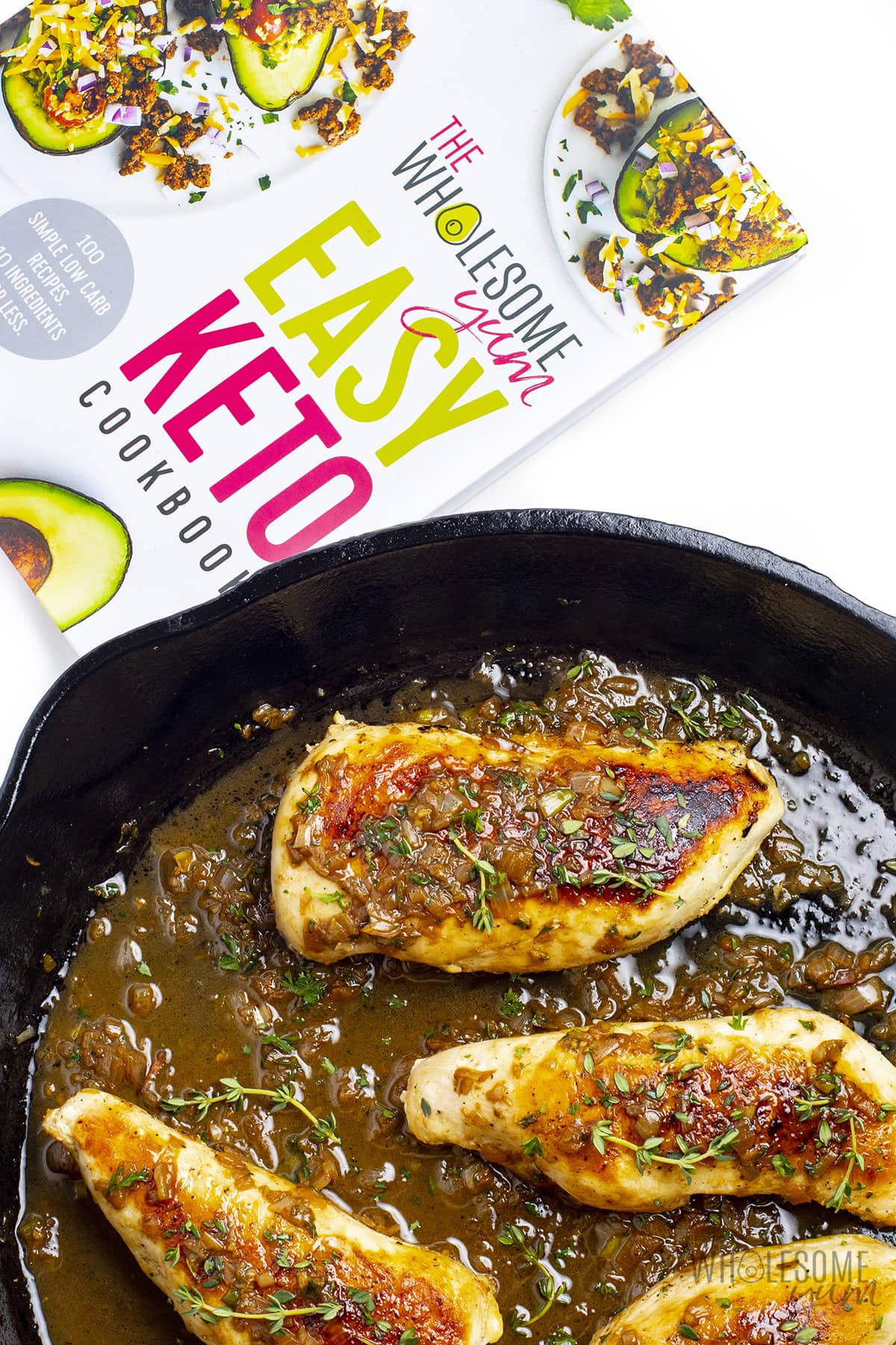 Sauteed chicken in a cast iron skillet next to Easy Keto Cookbook.