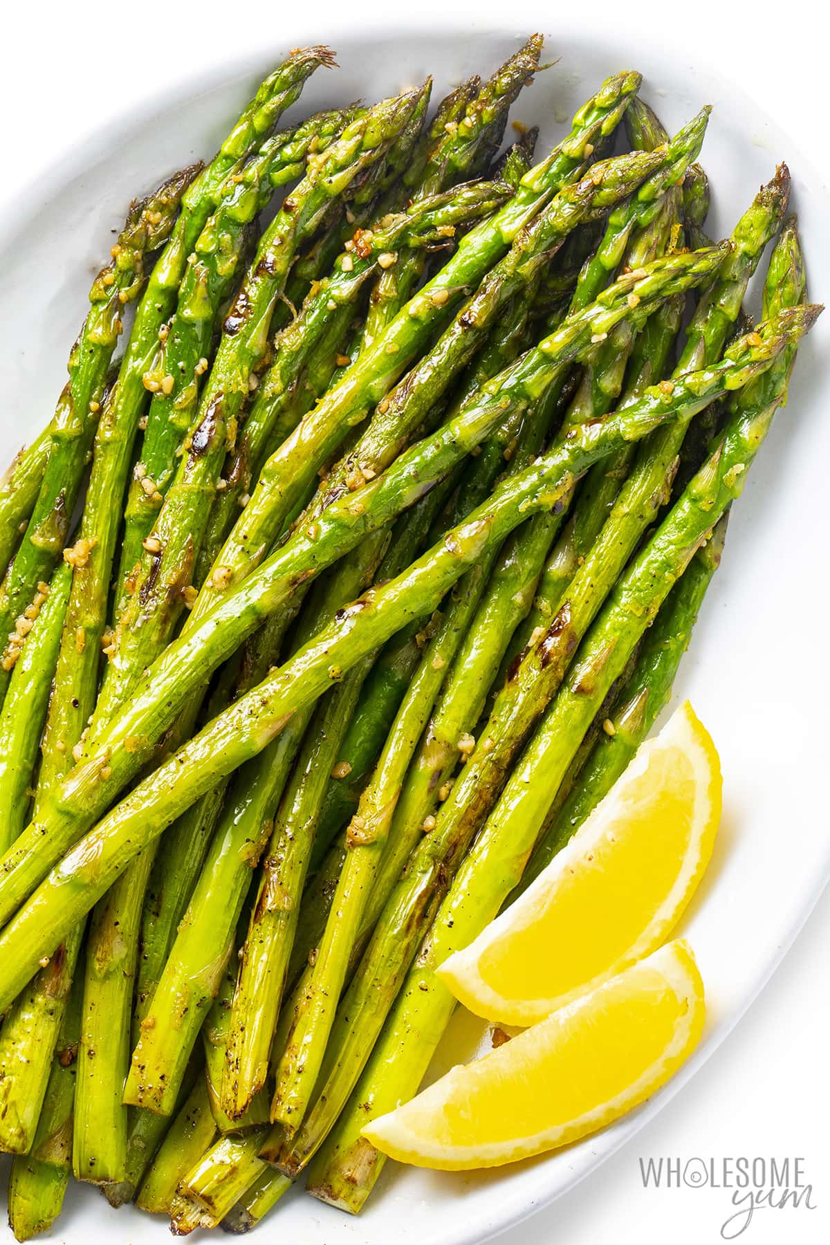 Sauteed asparagus on a plate with lemon wedges.
