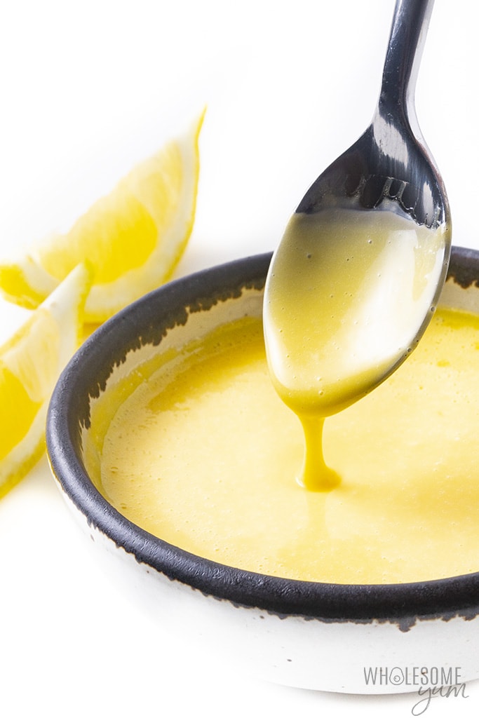 Bowl of hollandaise sauce with lemon wedges and a spoon