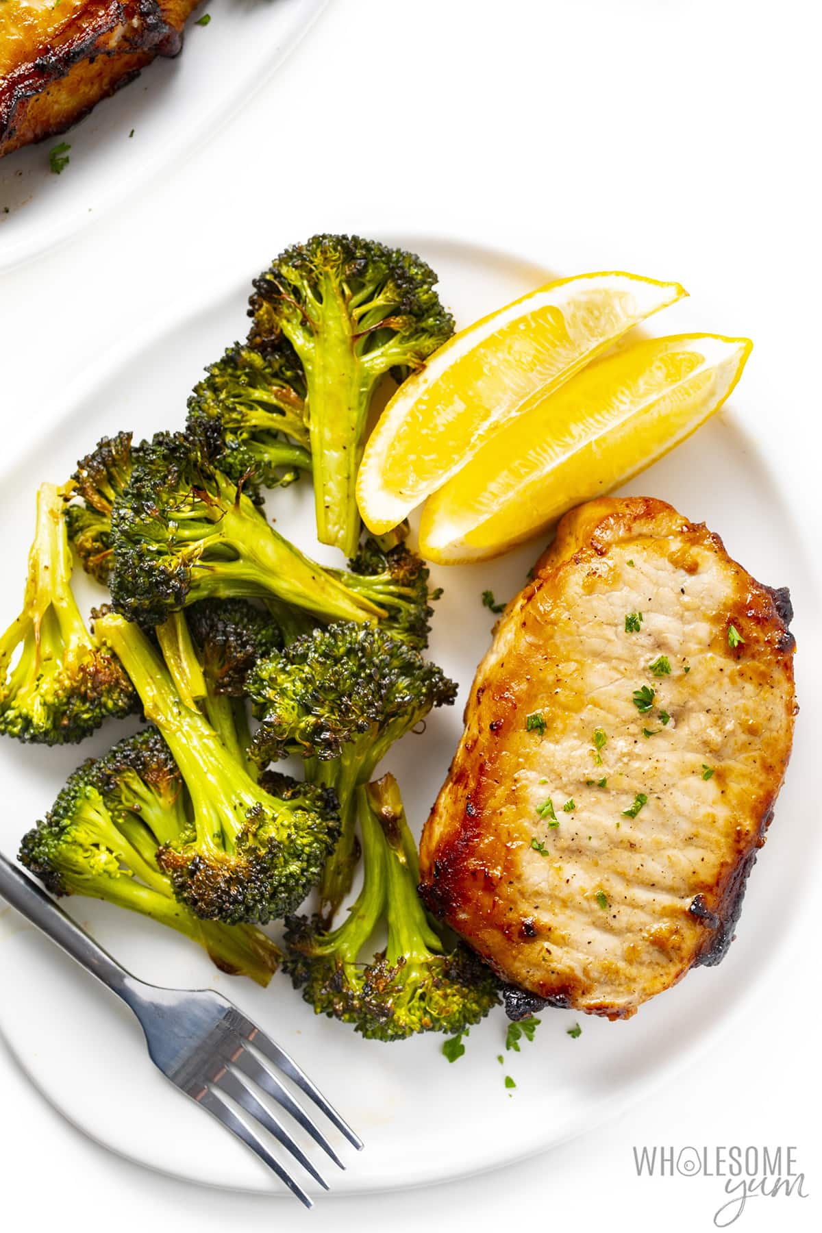 Air fryer boneless pork chops on a plate with roasted broccoli and lemon wedges.