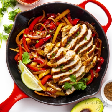 Chicken fajitas in a skillet with fresh cilantro and lime wedges.