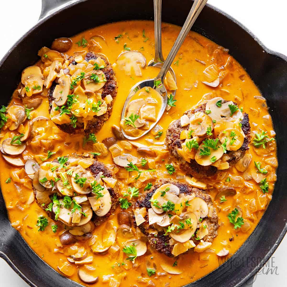 Easy Salisbury steak recipe in a skillet, with tender beef patties smothered in gravy and two spoons.