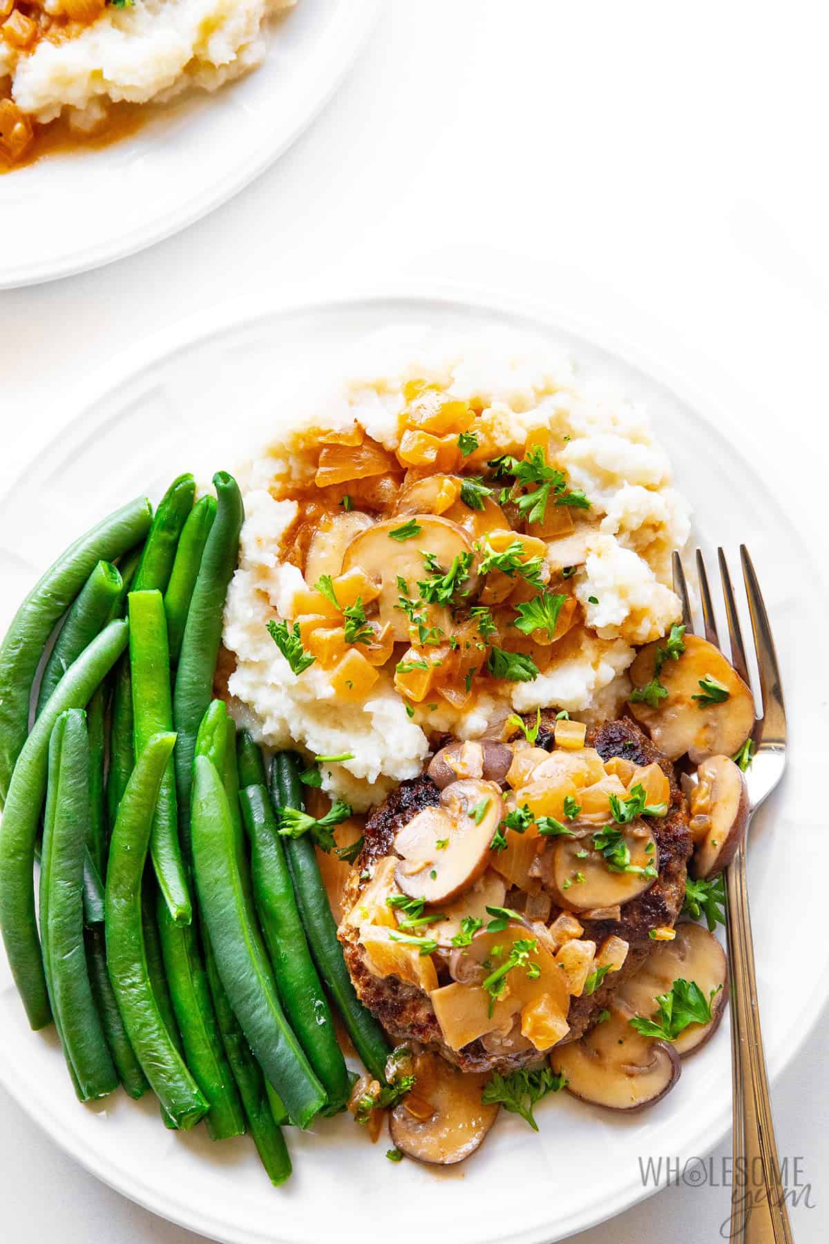 Tender salisbury steak and gravy on a plate with mash, green beans, and a fork.