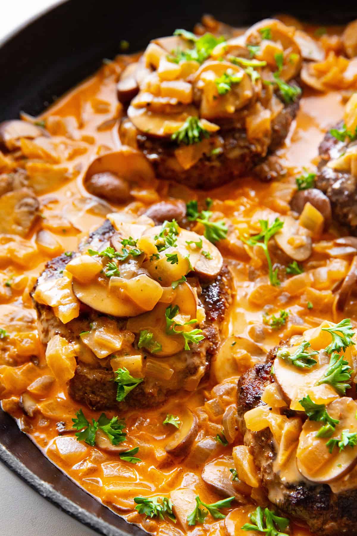 Juicy Salisbury steak in a skillet topped with rich, creamy mushroom gravy and a sprinkle of fresh parsley.