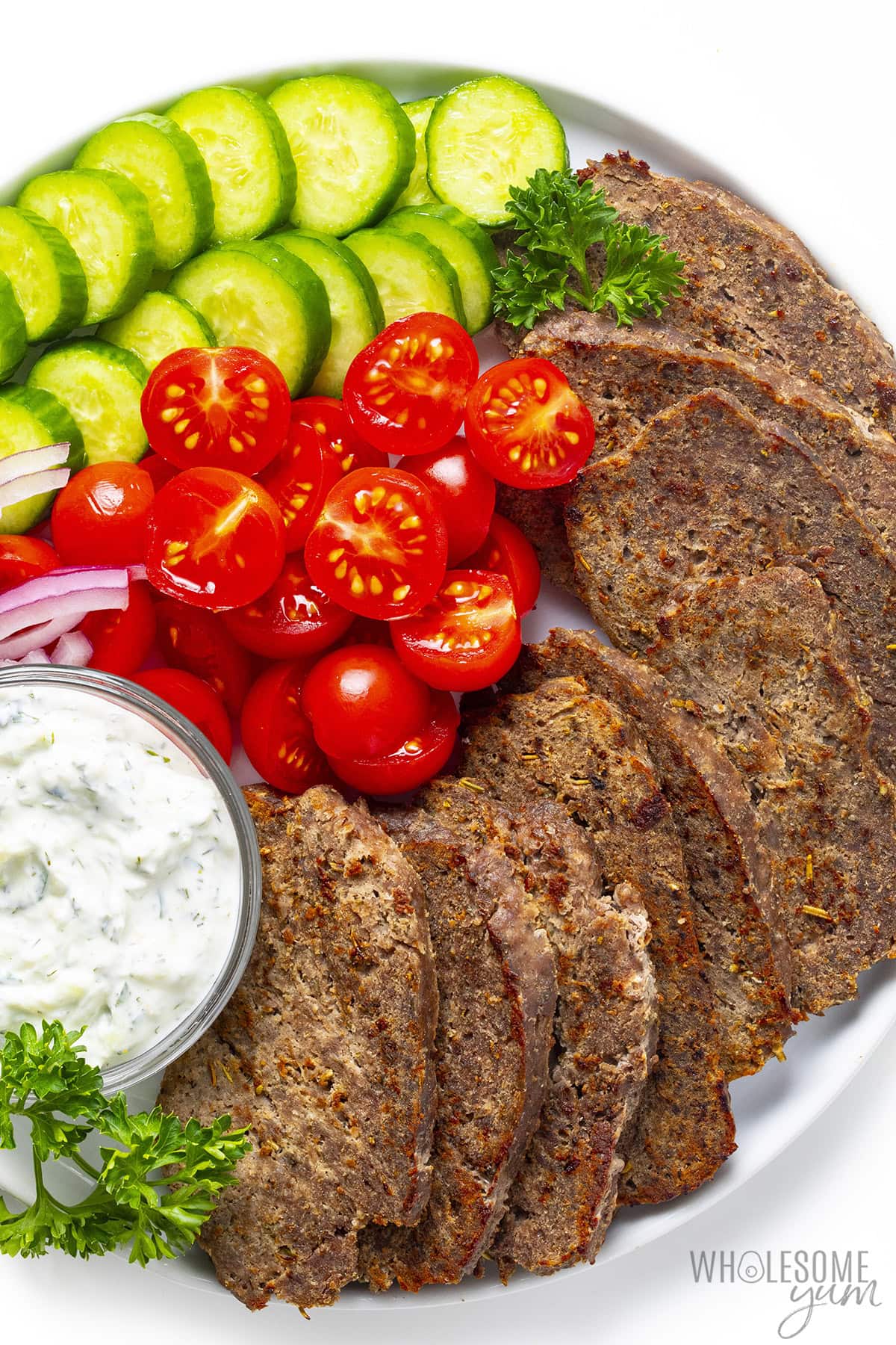 Sliced gyro meat on a platter with veggies and tzatziki sauce.