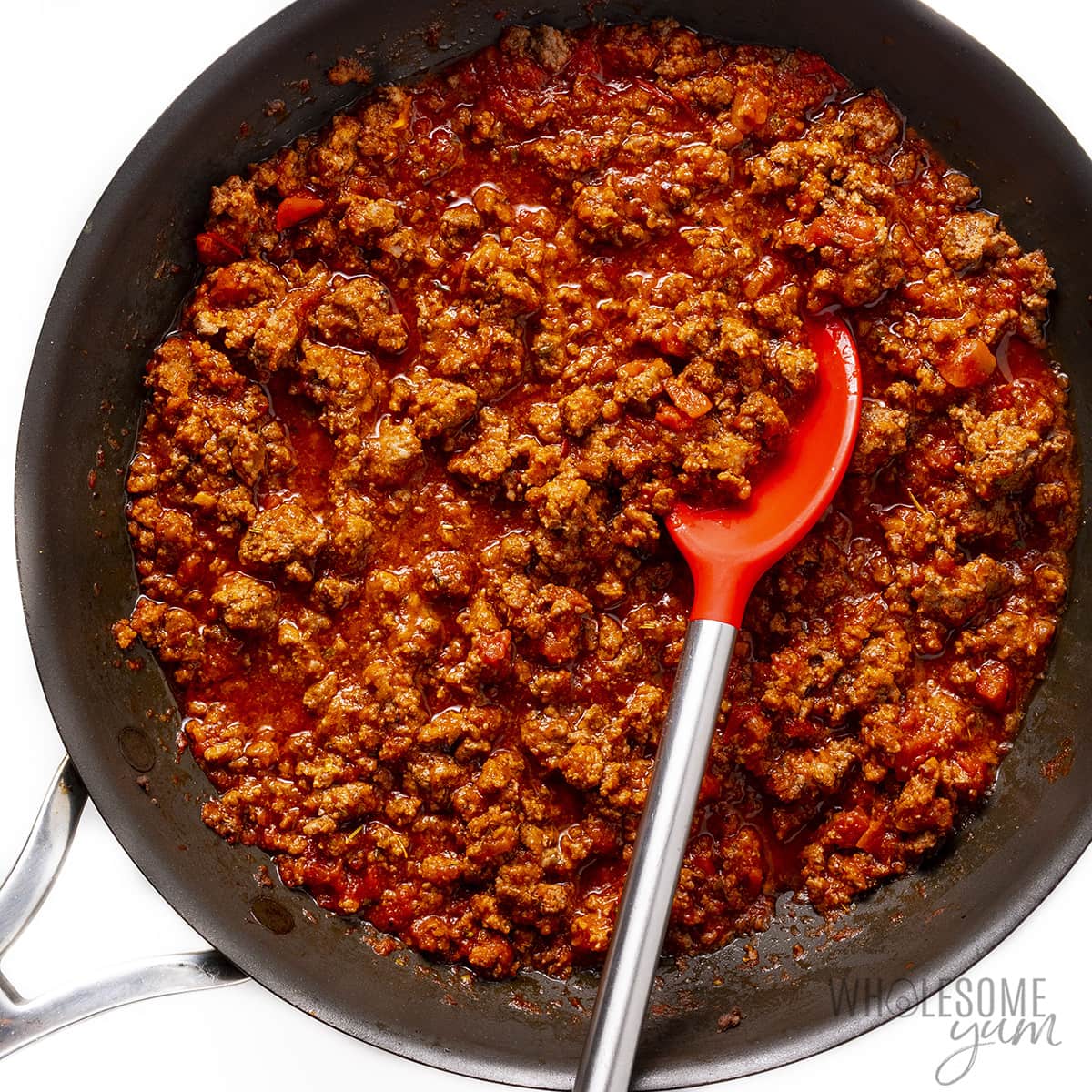 Meat sauce in a skillet with a spoon.