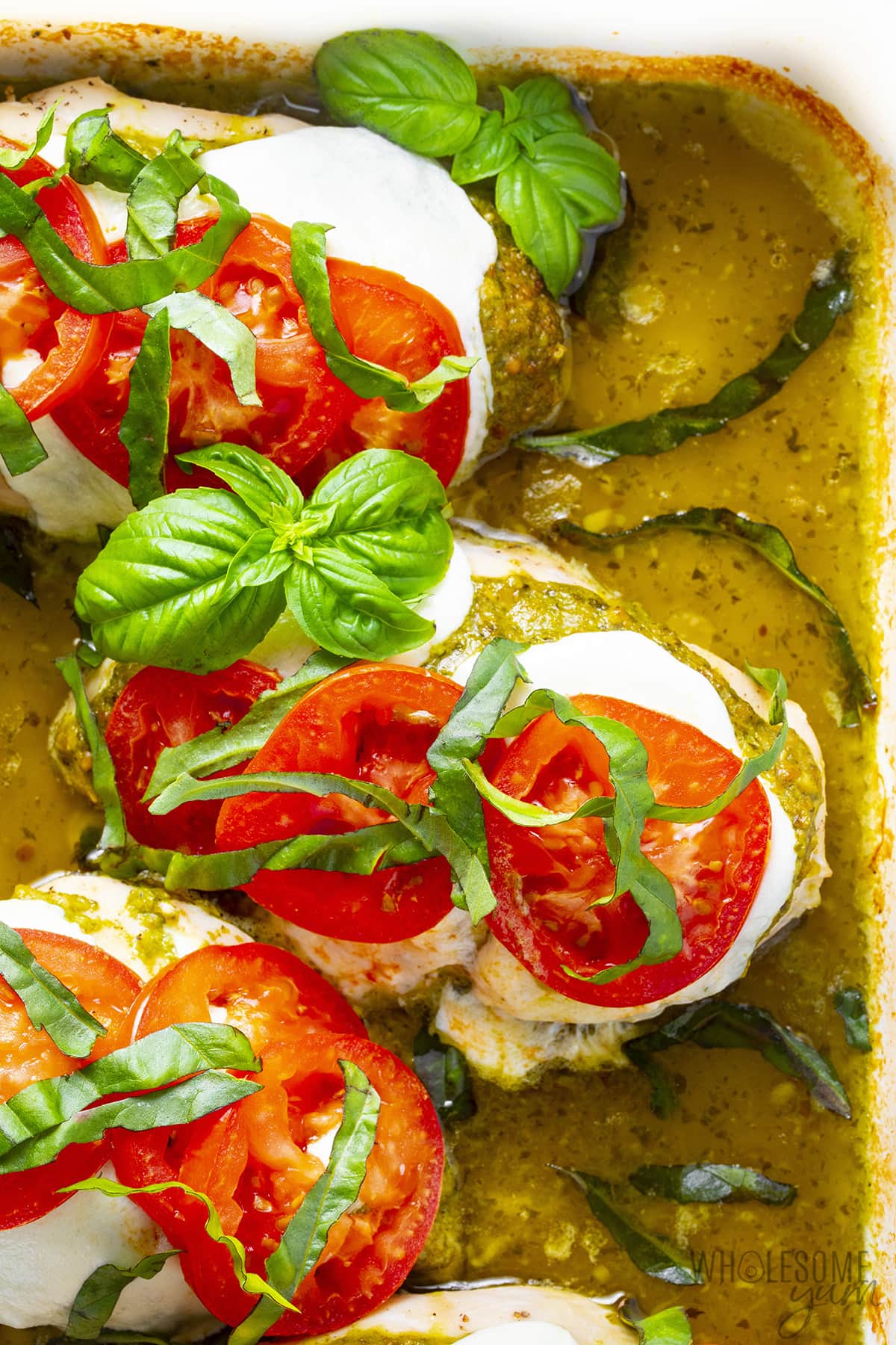 Pesto chicken with mozzarella, sliced tomatoes, and fresh basil in a baking dish.