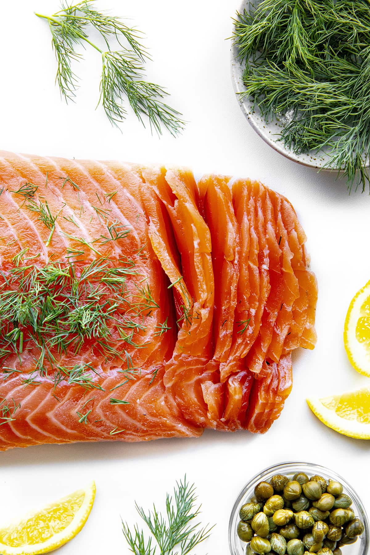 Salmon lox cut into thin strips next to fresh dill and lemon wedges.