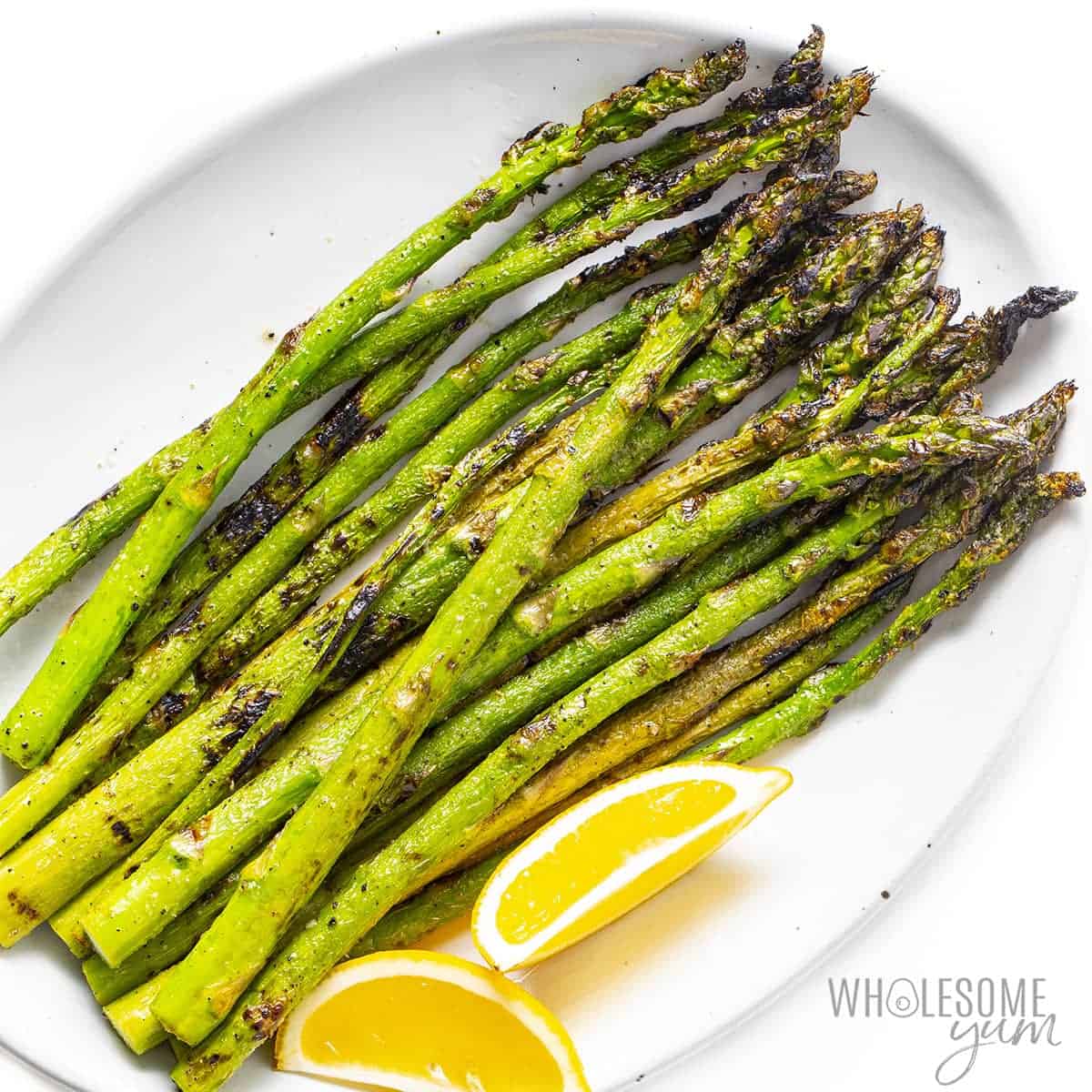 Grilled asparagus spears on a plate with lemon wedges