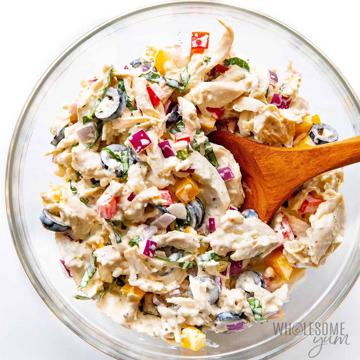 Mediterranean chicken salad mixed in a bowl with a wooden spoon.