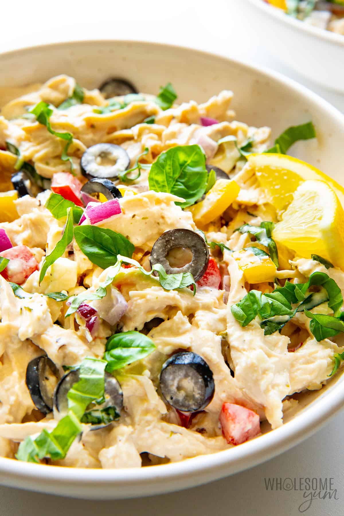 Creamy, colorful Mediterranean chicken salad in a bowl with lemon wedges and fresh basil.