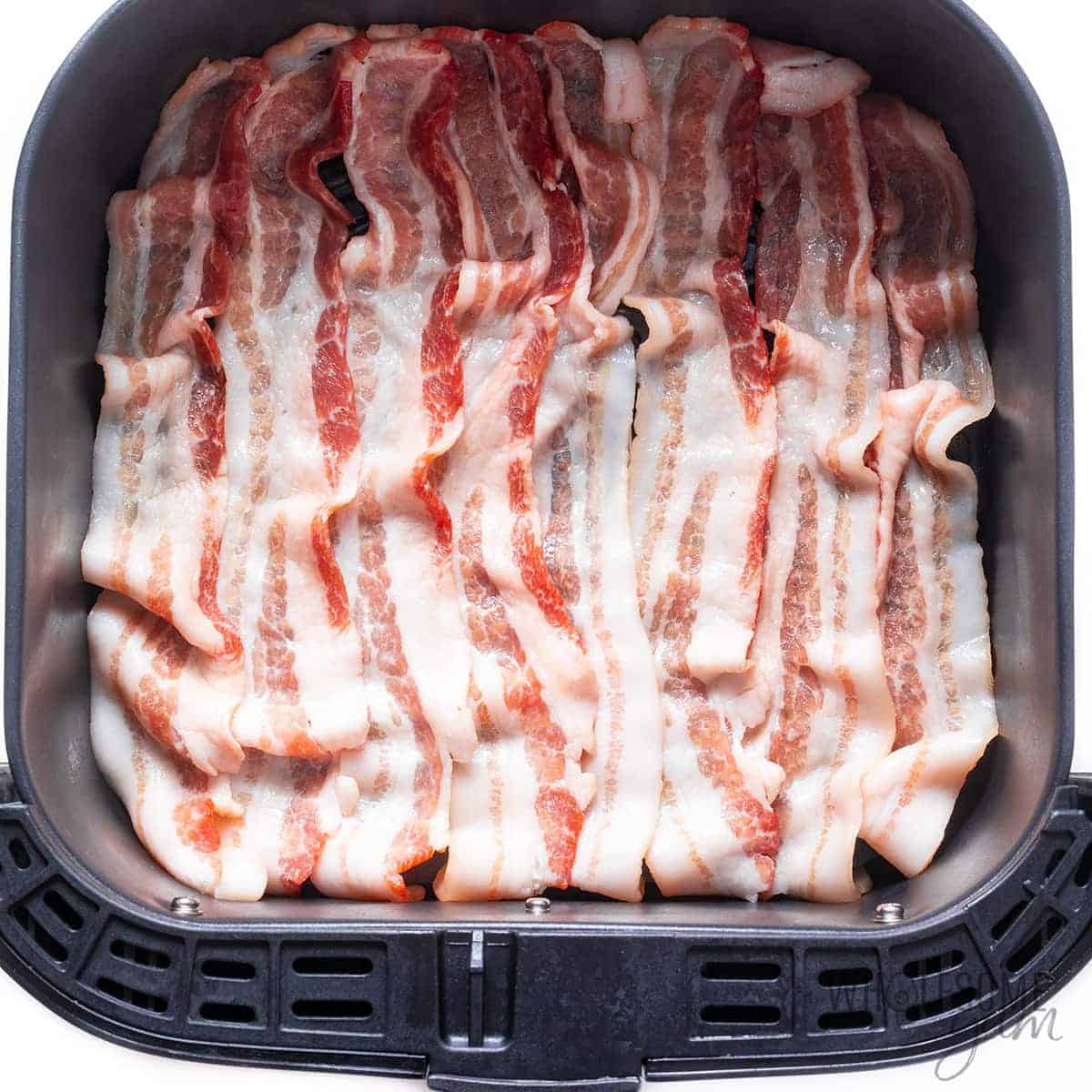 Raw bacon strips in air fryer basket.