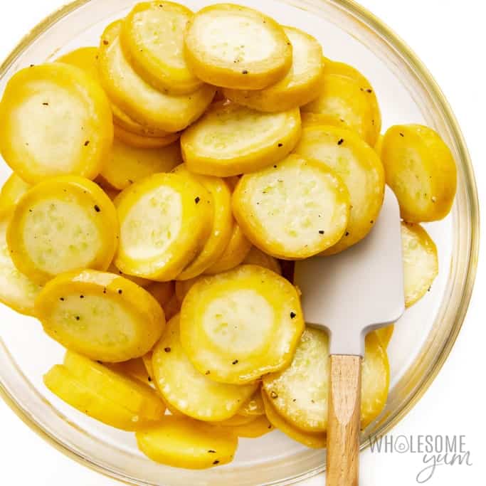 Sliced summer squash in a bowl with seasonings.