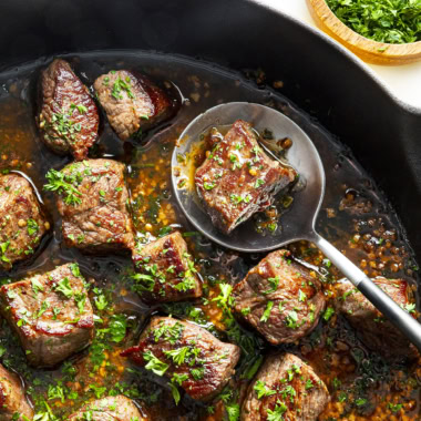 Garlic butter steak bites in a skillet with a spoon.