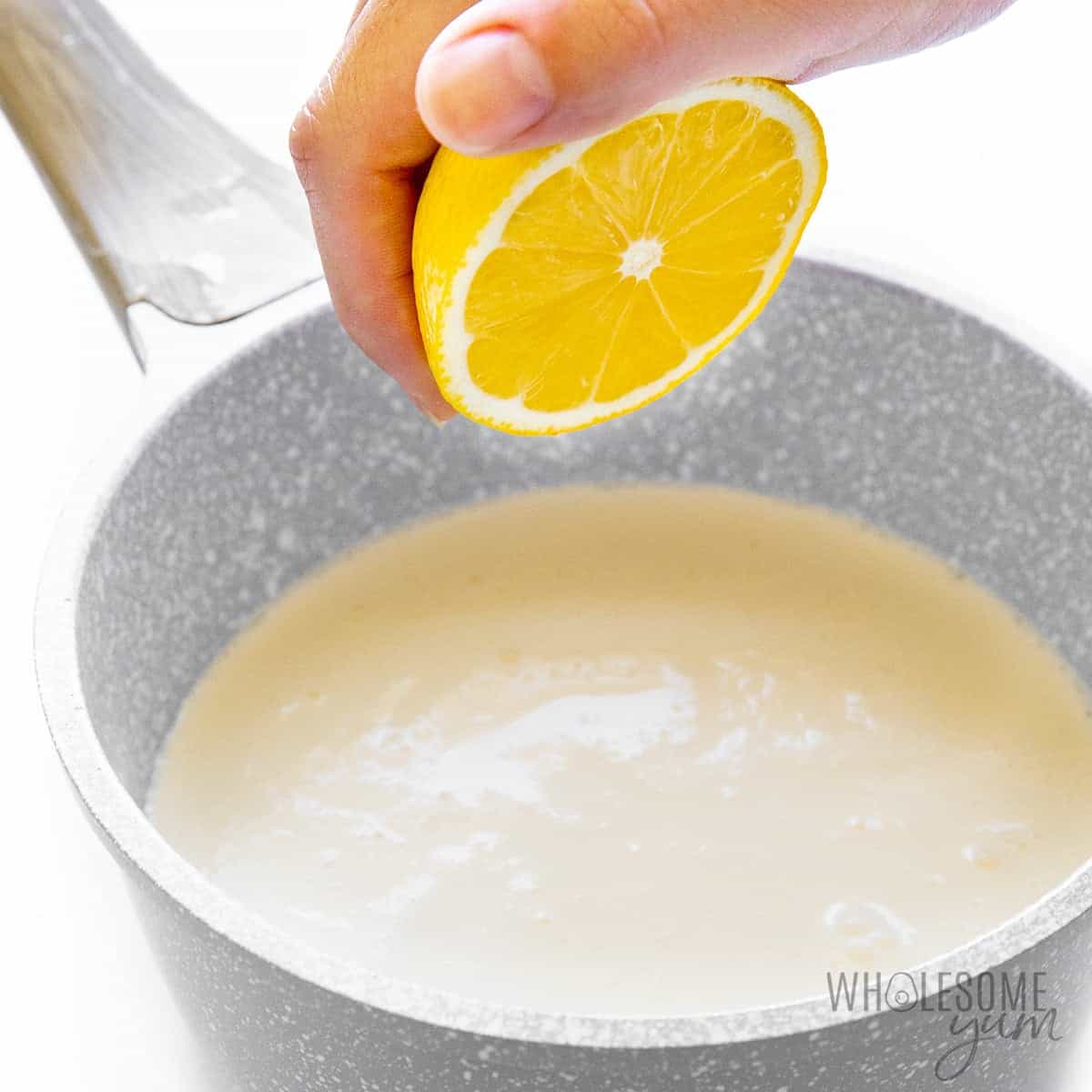 Hand squeezing a lemon over cream in saucepan