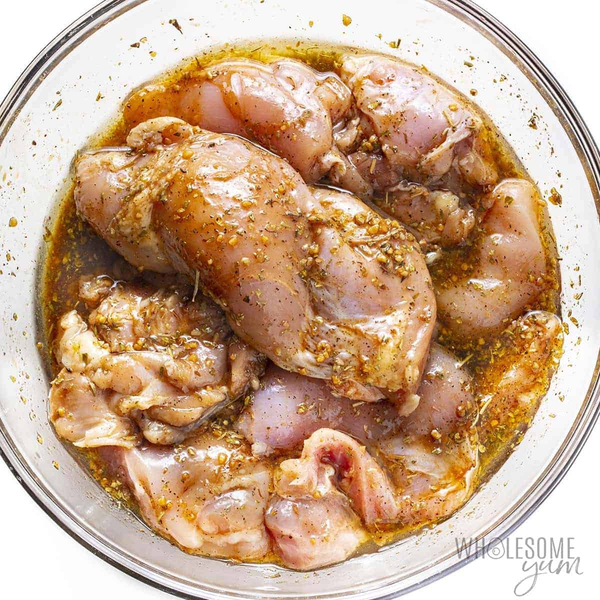 Raw chicken thighs in a bowl with Mediterranean chicken marinade.