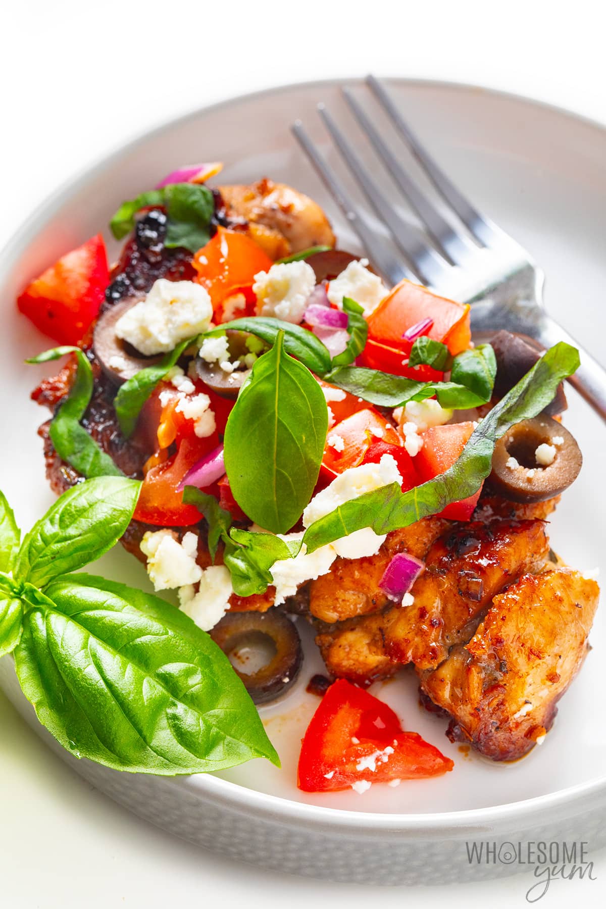 Mediterranean chicken on a plate with fresh basil and a fork.