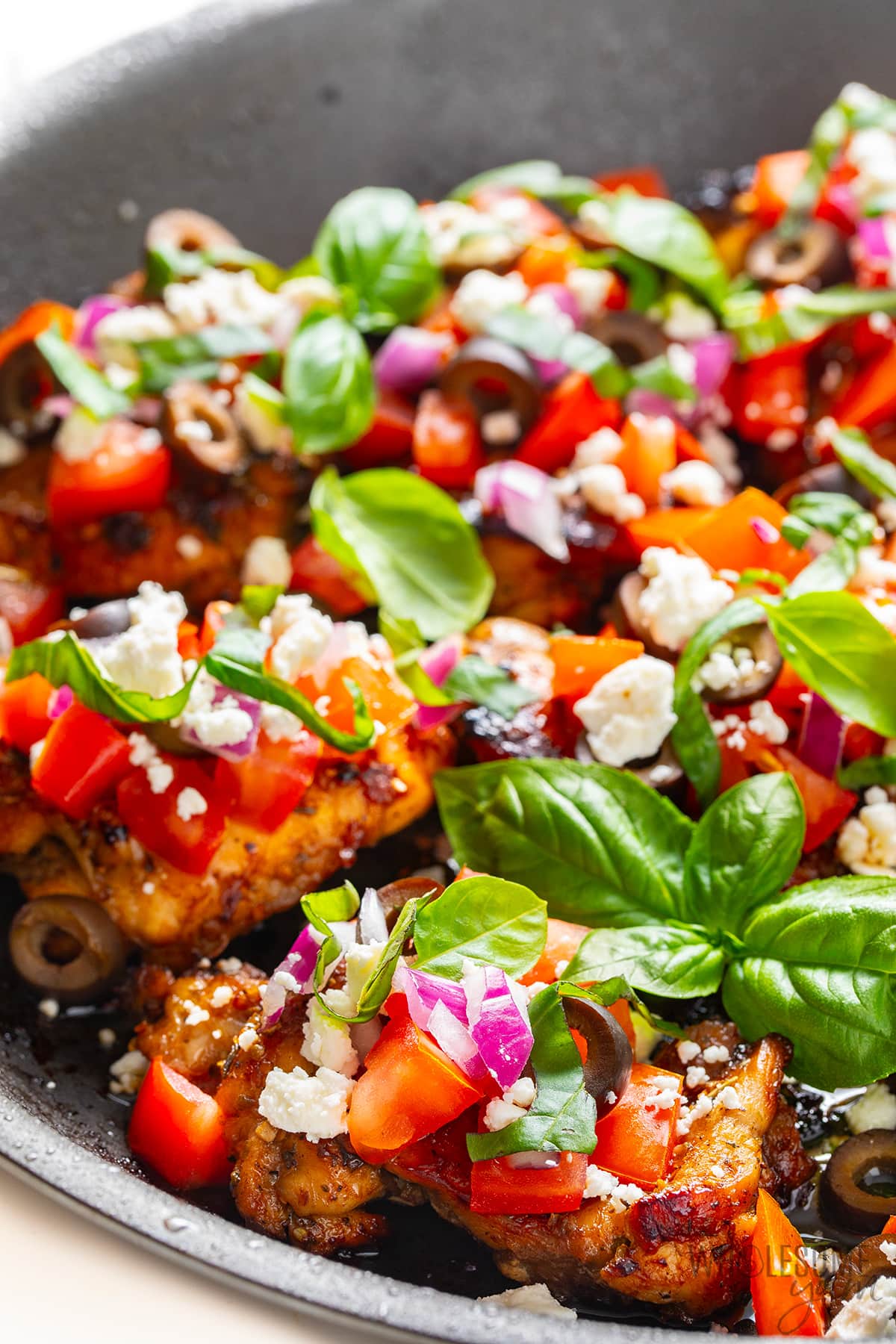 Mediterranean chicken recipe with toppings and fresh basil leaves in a pan.