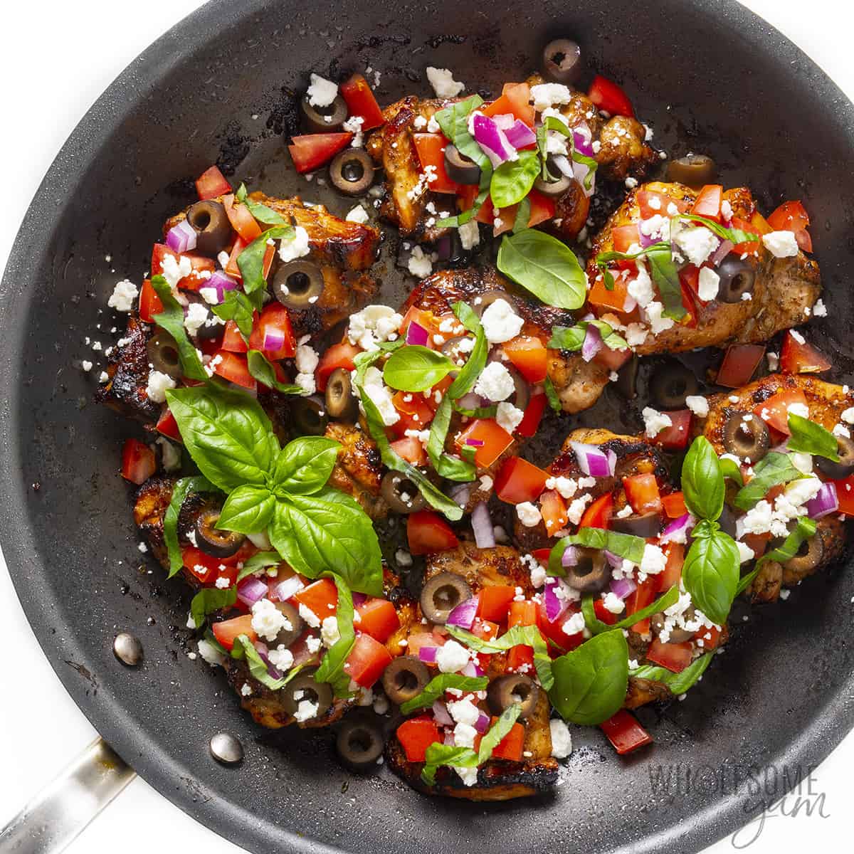 Mediterranean chicken recipe in a skillet with toppings and fresh basil added.