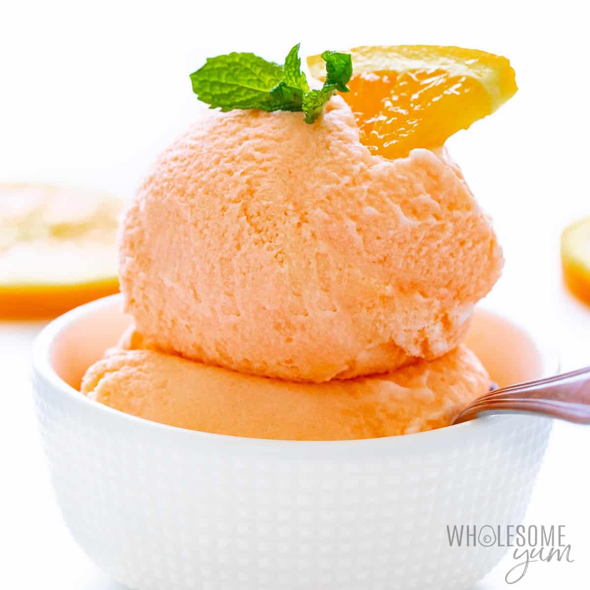 Scoops of keto sherbet in a bowl with orange segment and mint sprig
