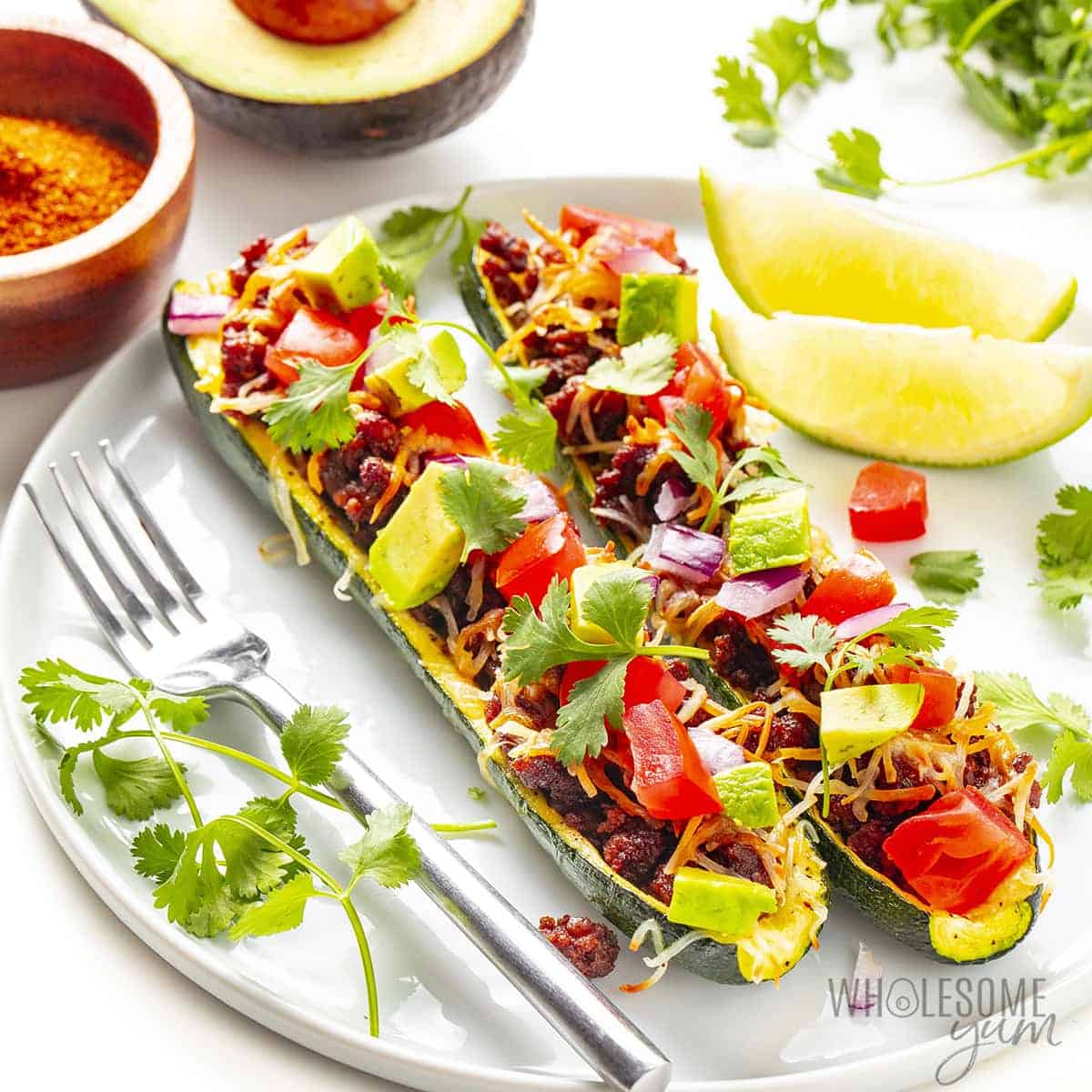 Zucchini taco boats on a plate with cilantro and limes