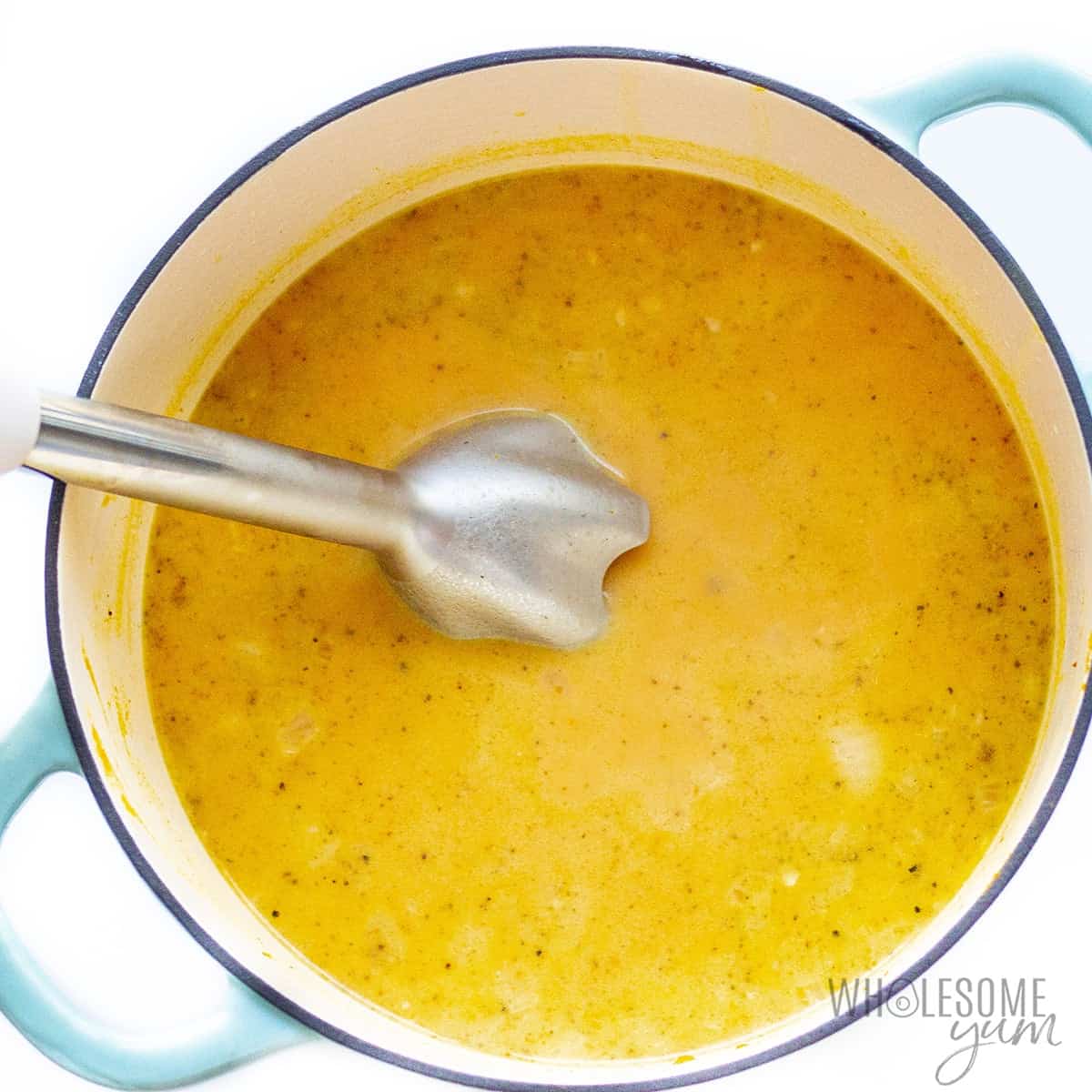 Immersion blender blending pumpkin soup in dutch oven