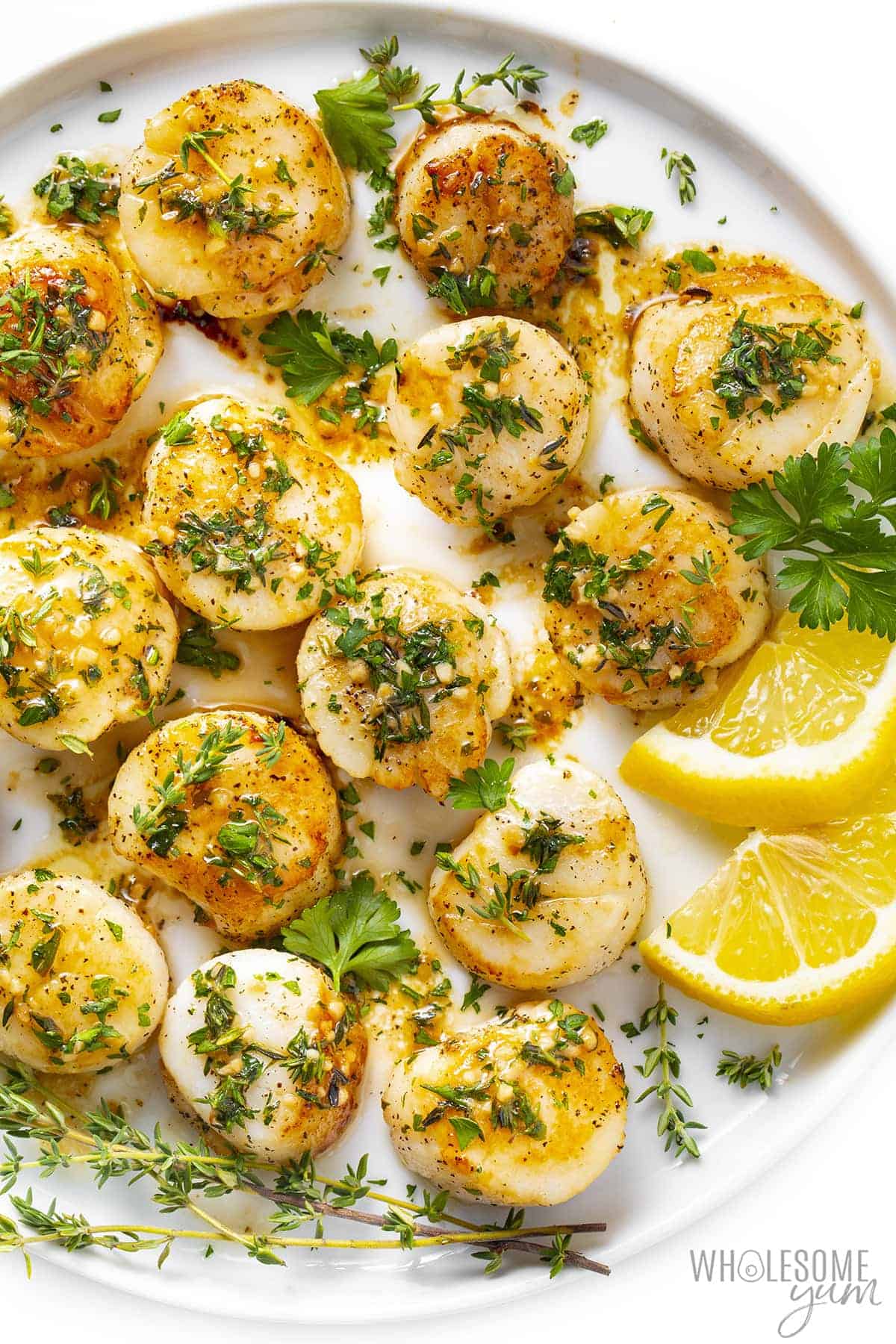 Plate of garlic butter scallops with lemon wedges and fresh herbs