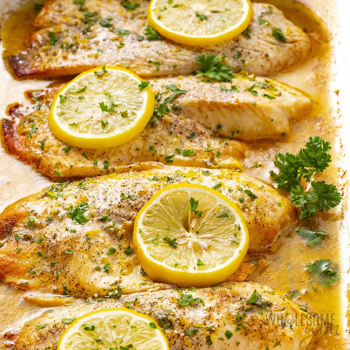Oven baked tilapia in a baking dish garnished with parsley.