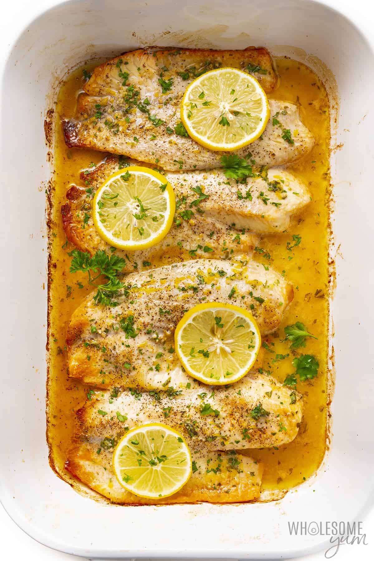 Baked tilapia recipe in a baking dish with lemon slices.